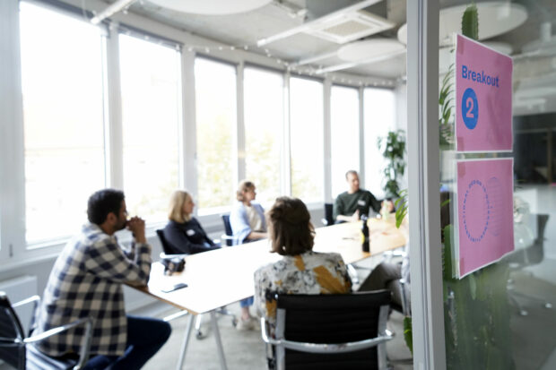 Participants of the community afternoon meetup at the German Federal Government Digital Service's office. 7 people are sitting around a conference table and conversing in a meeting room. Everyone is a bit blurred and overexposed because the sun is streaming directly into the room. 