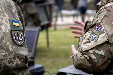 Two sleeves of soldiers are visible, featuring the flags of UK and Ukraine.