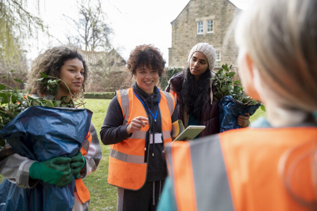 4 female volunteers in high vis carrying bags of garden waste.