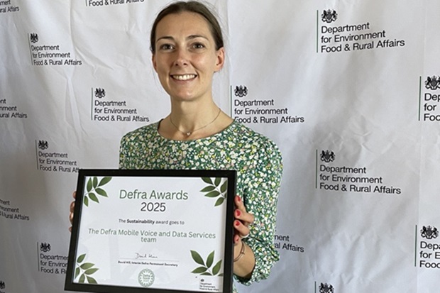 A lady wearing a green flowered dress holds up a certificate in a frame which says Defra Awards 2025.